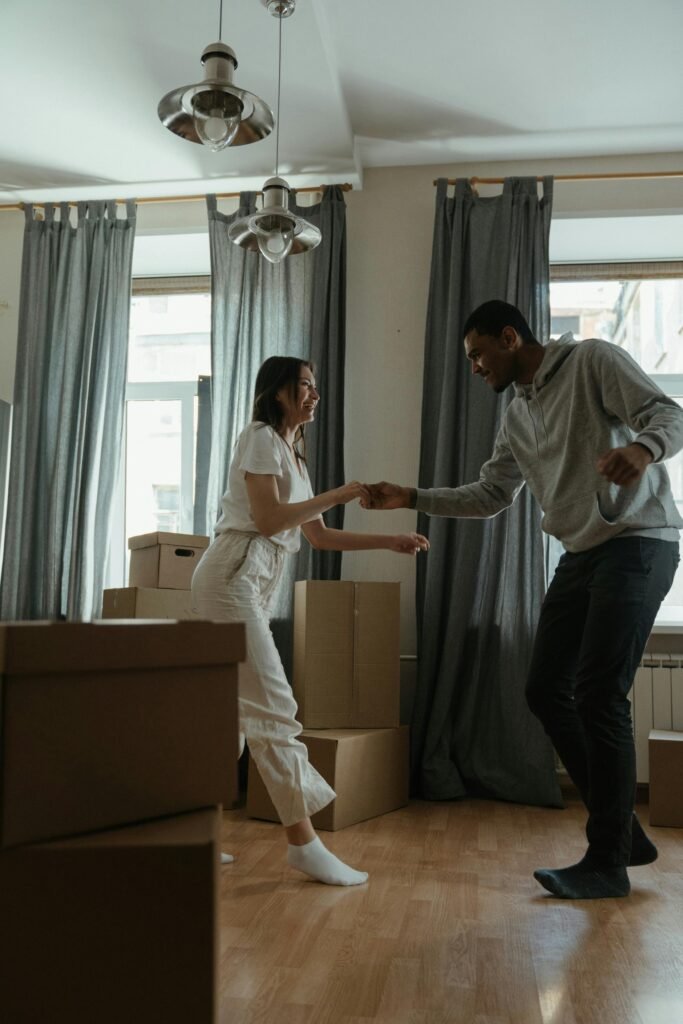 Happy couple dancing among cardboard boxes in their new home, celebrating a fresh start.